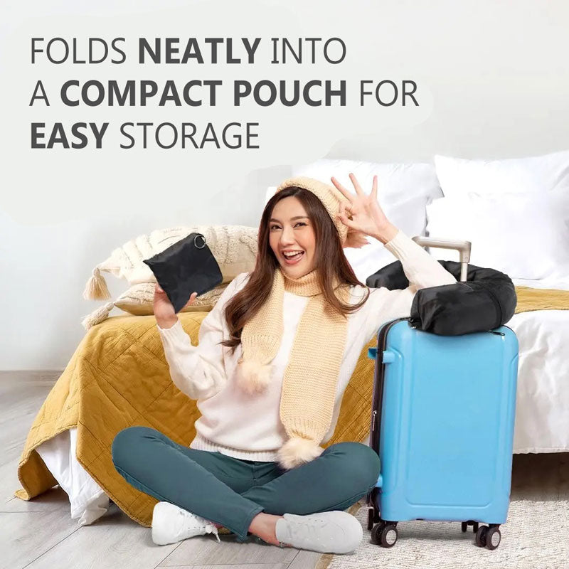 Smiling Asian woman holding a folded GoTripps Stuffable Travel Neck Pillow in one hand, with the other hand doing an OK sign and arm rested on a blue suitcase