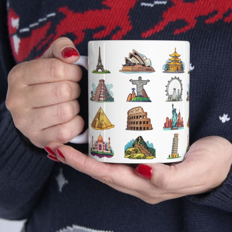 White ceramic coffee mug featuring famous world travel landmarks, cradled by the delicate hands of a person wearing a cozy Christmas blue and red sweater