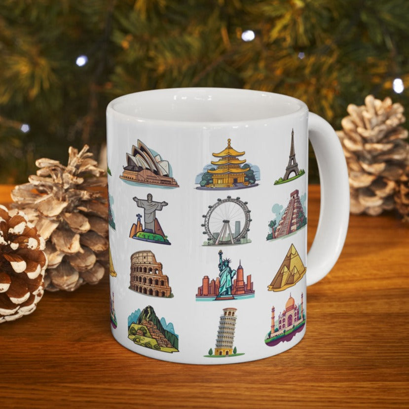 White ceramic coffee mug featuring famous world travel landmarks, on a wooden table with Christmas decoration