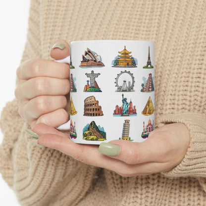 white ceramic coffee mug featuring famous world travel landmarks, held by feminine hands wearing a beige sweater