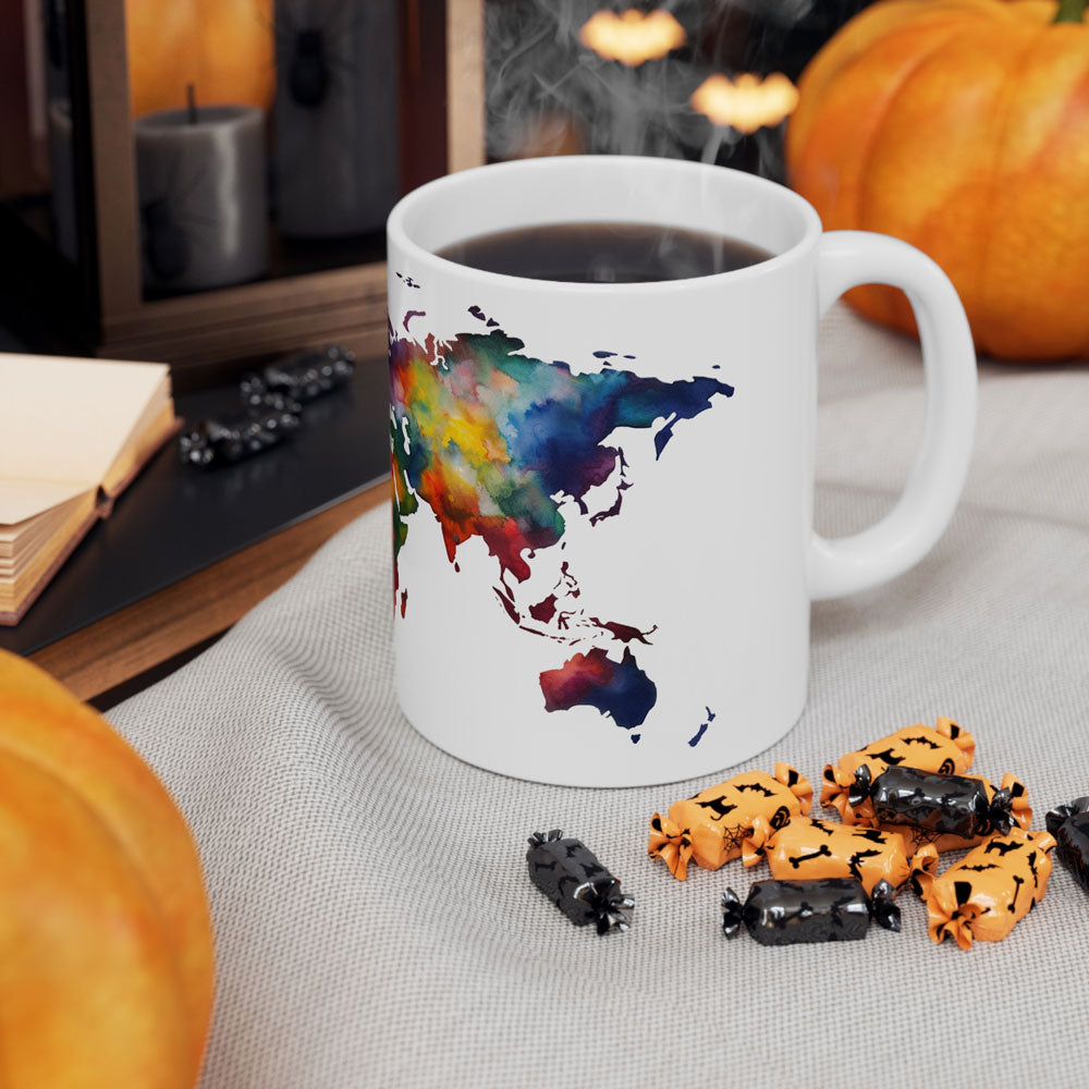 White ceramic coffee mug featuring a color world map, on a table with white cloth, next to pumpkins and other Halloween decoration