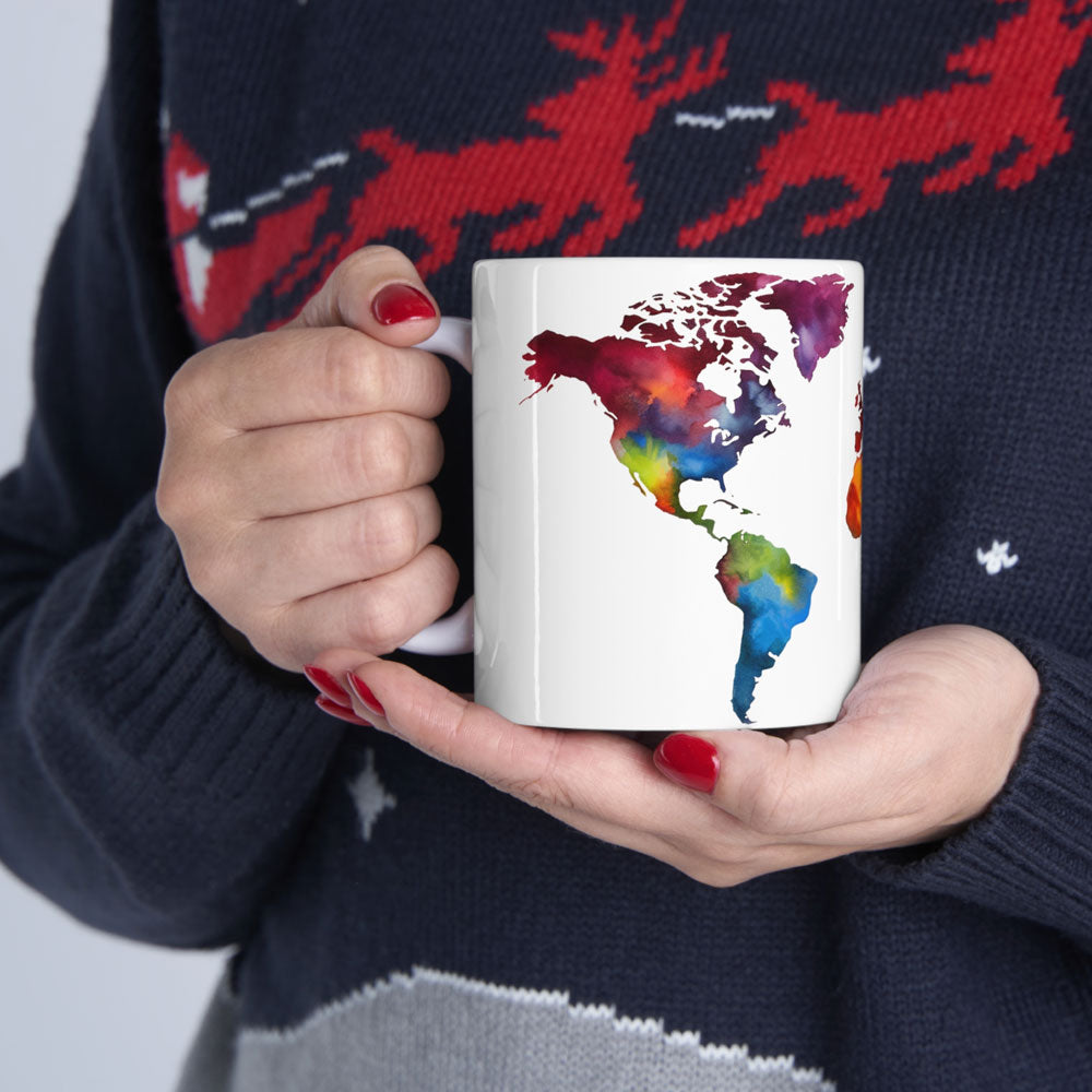 White ceramic coffee mug adorned with a vibrant world map design, cradled by the delicate hands of a person wearing a cozy blue and red sweater