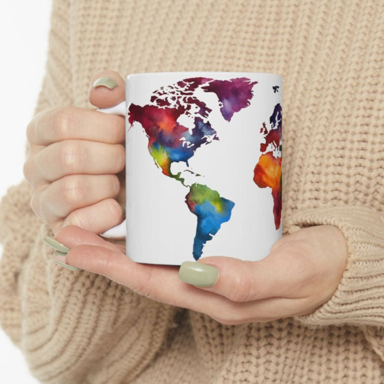 white ceramic coffee mug featuring a color world map, held by feminine hands wearing a beige sweater