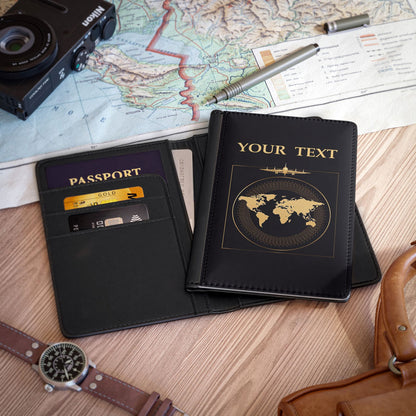 Two black leather passport covers with custom world map design, one closed and the other open with displayed credit cards, on a wooden table with travel accessories and decorations