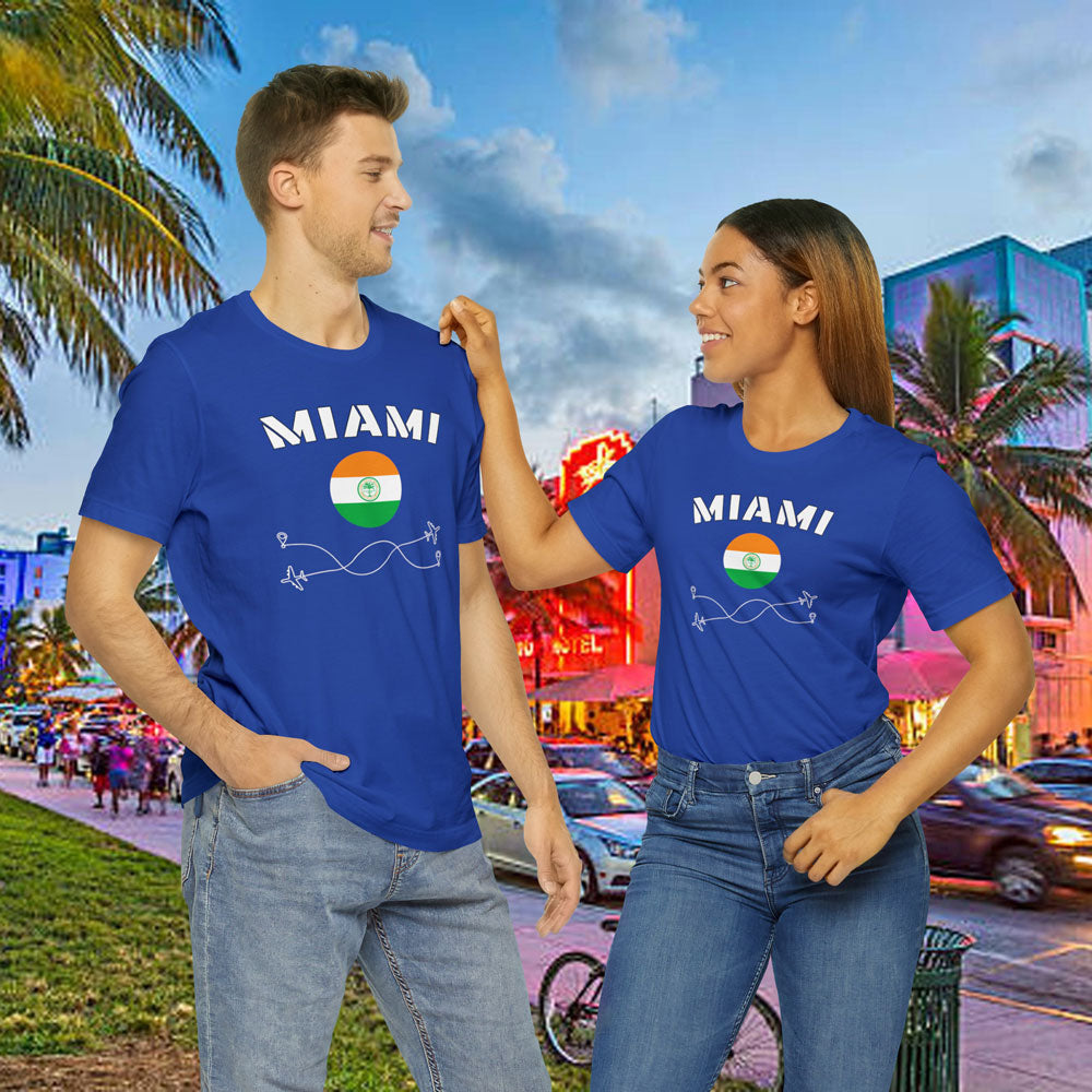 White man and brown woman wearing a blue cotton T-shirt featuring the word 'Miami' and its rounded flag. The background shows Miami Beach's Ocean Drive