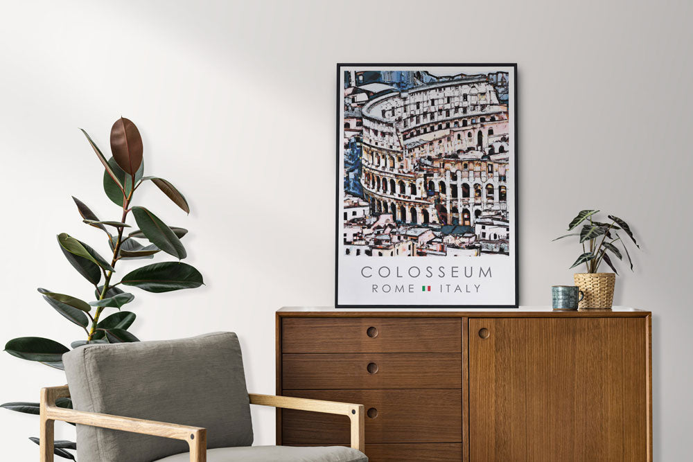 Black-Framed poster of the Colosseum in Italy on a white wall above a wooden cabinet in a decorated room with a gray chair and plants