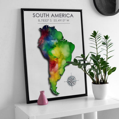 Black-framed poster featuring a colorful map of South America, elegantly displayed against a clean white wall, on a sleek white table, next to a plant and other decoration