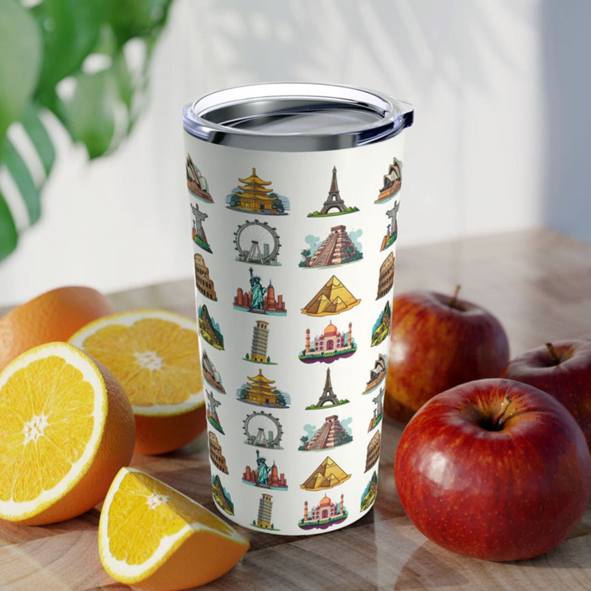 20oz white tumbler featuring famous travel landmarks resting on a brown table surrounded by oranges and apples
