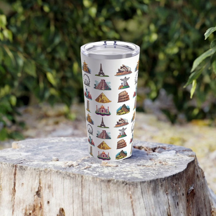 20oz white tumbler featuring famous travel landmarks resting on a tree stump surrounded by plants