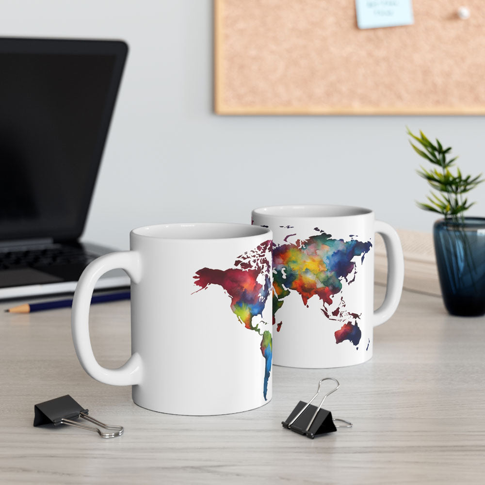 two white ceramic coffee mugs featuring a color world map, on a light gray office table next to a computer and other decoration 